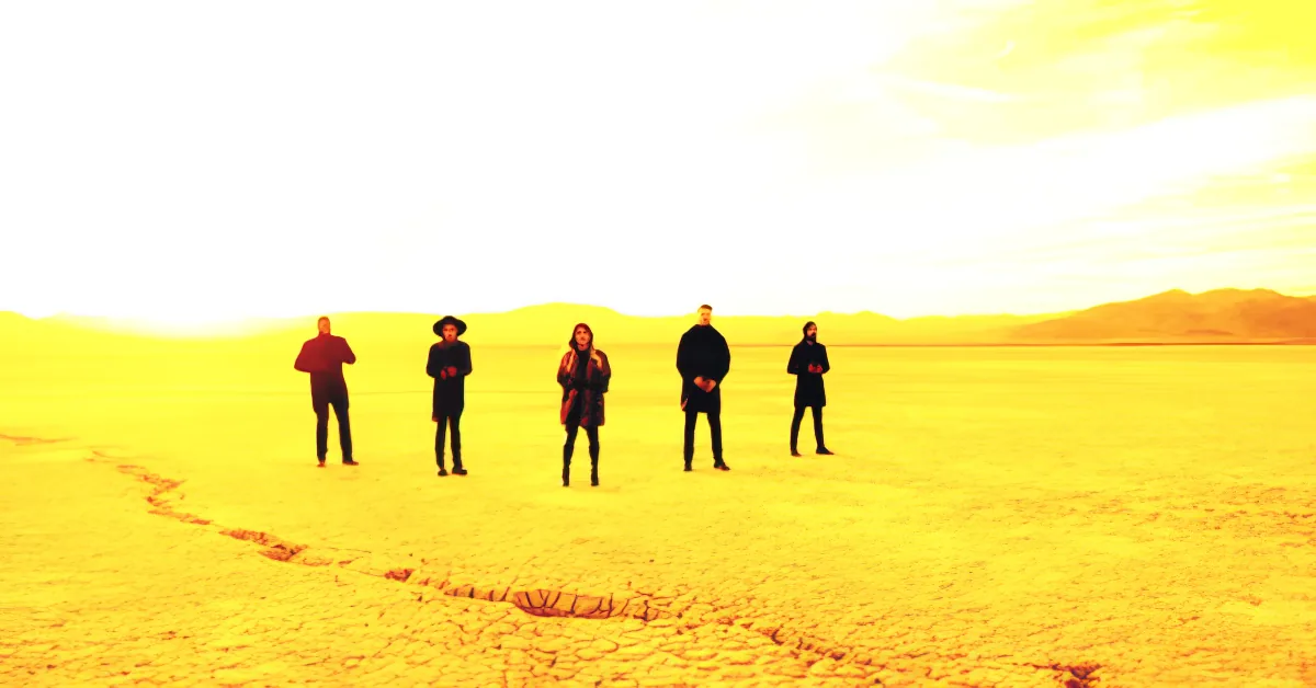 A group of people stands in a vast, sunlit desert landscape with a bright sky.
