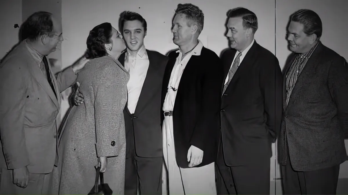 Elvis Presley is surrounded by five men in a group photo, dressed in suits and casual attire.