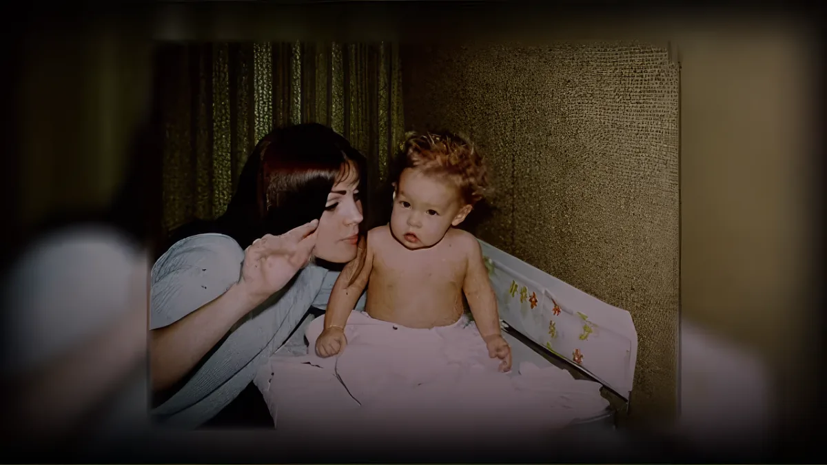 A woman holds a baby in a crib, both looking at something off-camera.
