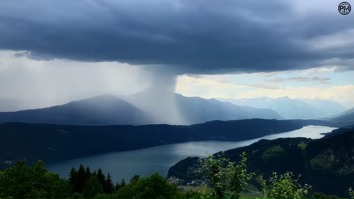 A dramatic stormy sky with rain clouds over a mountainous landscape and a lake.