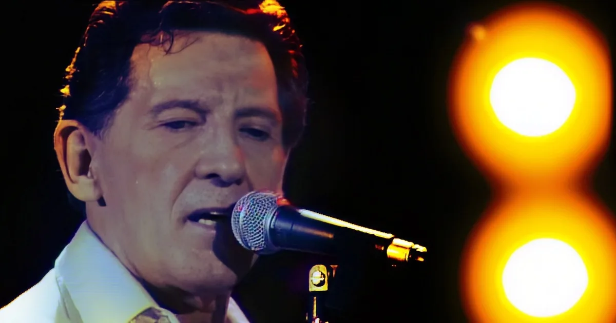 A man sings into a microphone with a dramatic lighting effect and a bright number 8 in the background.