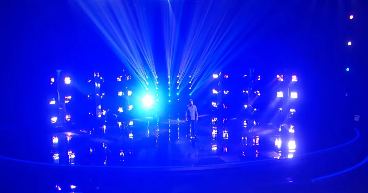 A person stands on a stage illuminated by bright blue lights and beams of light.