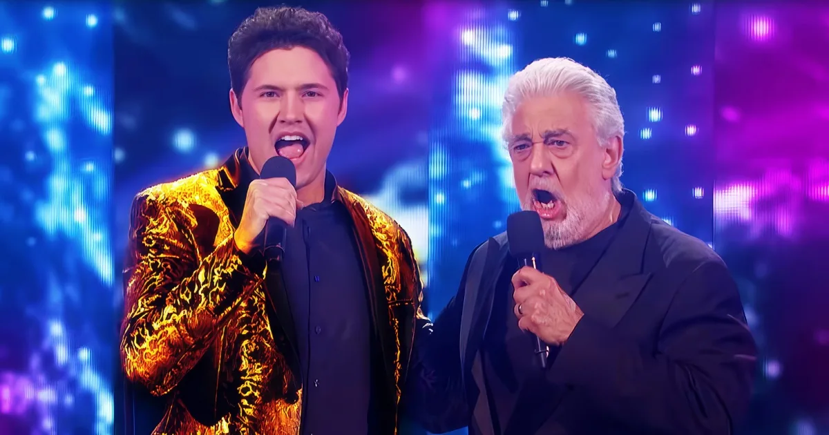 Two men, one in a gold jacket and the other in black, sing passionately on stage with vibrant blue and purple lights.