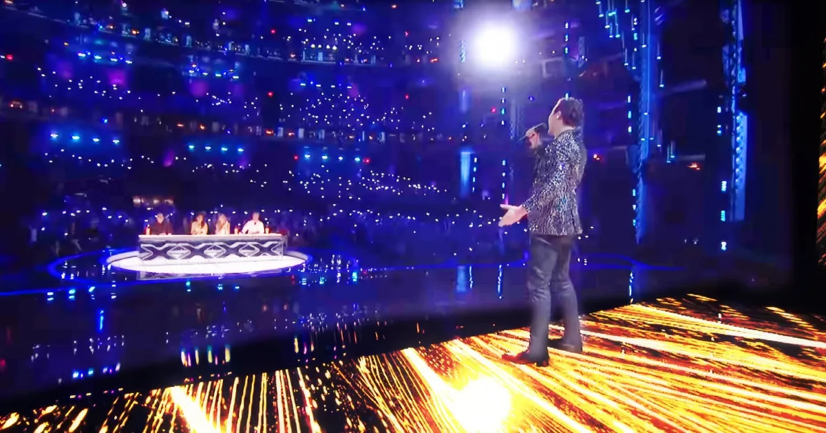 A performer sings on a stage with vibrant lights and a glowing floor, while judges sit at a table in the background.