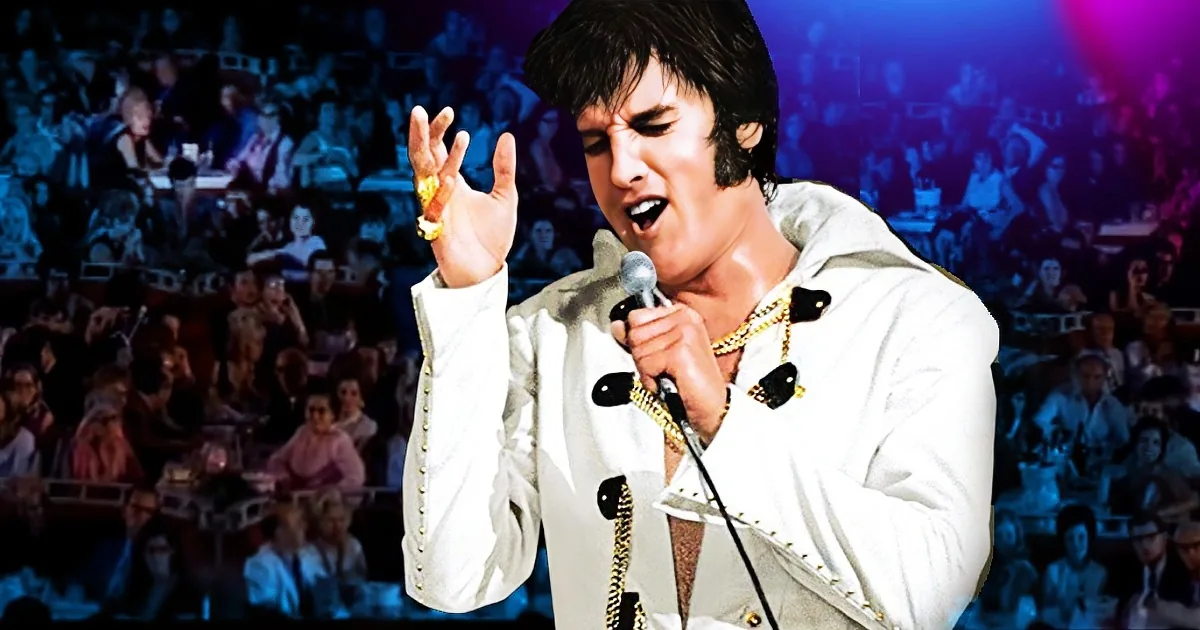 Elvis Presley in a white suit, holding a microphone, performing on stage with a crowd in the background.