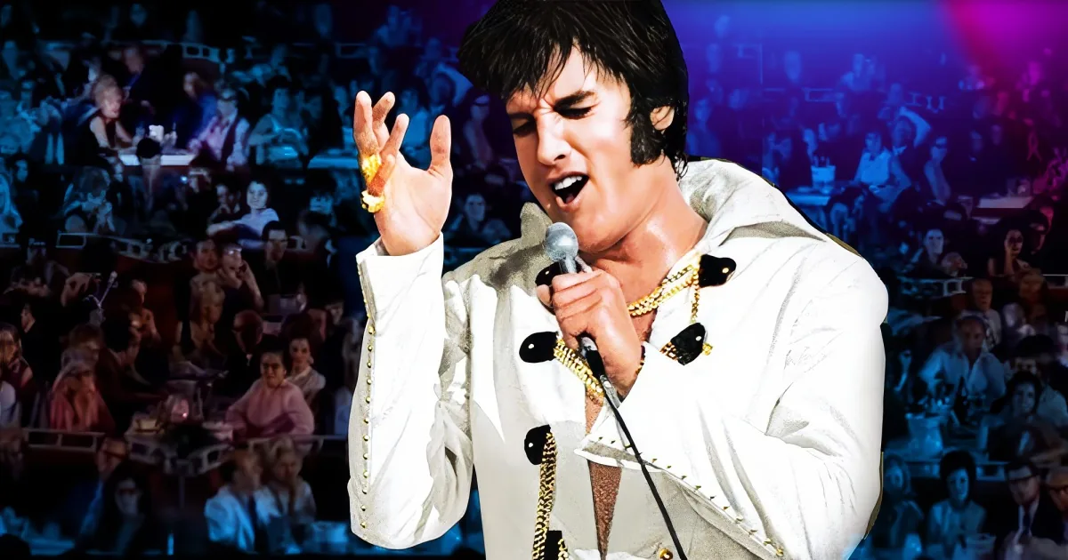 A performer in a white outfit with gold chains holds a microphone, gesturing with one hand.