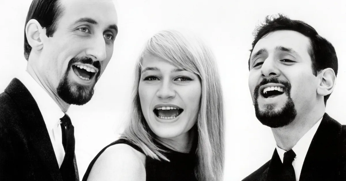 A black-and-white image shows three people, two men and a woman, laughing and smiling.