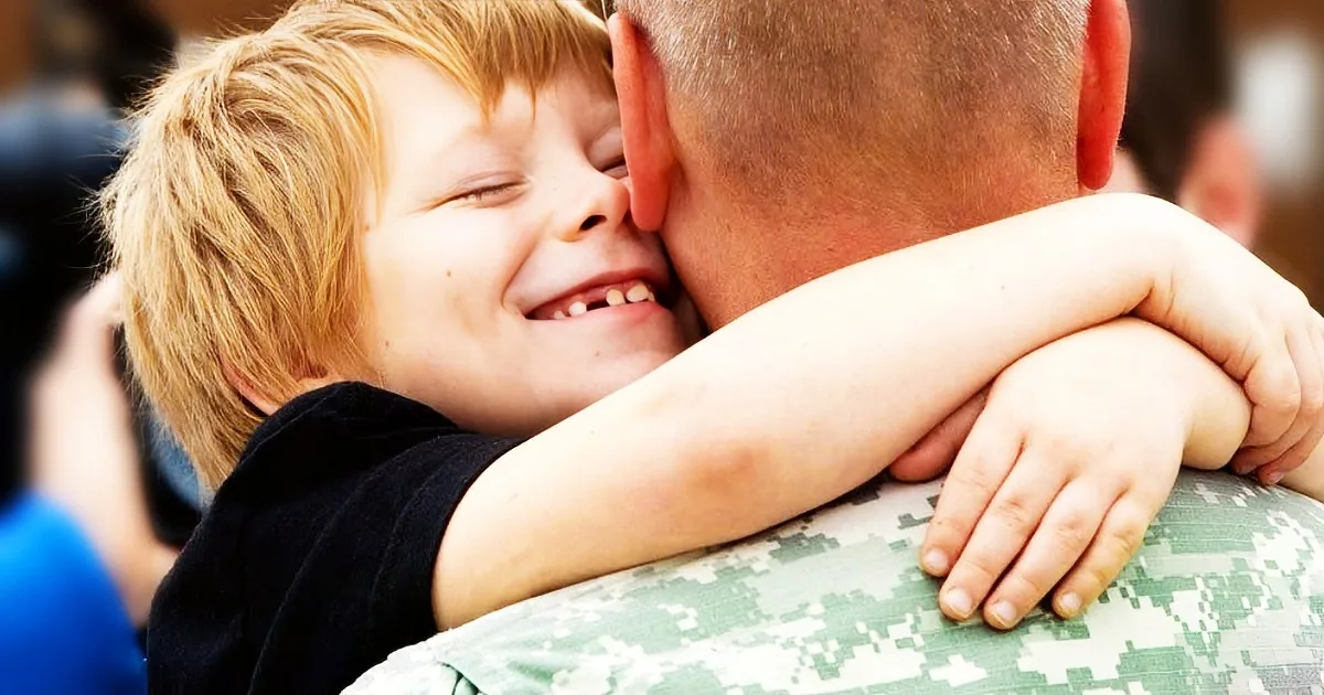 A young boy hugs a soldier in a military uniform, both smiling warmly.