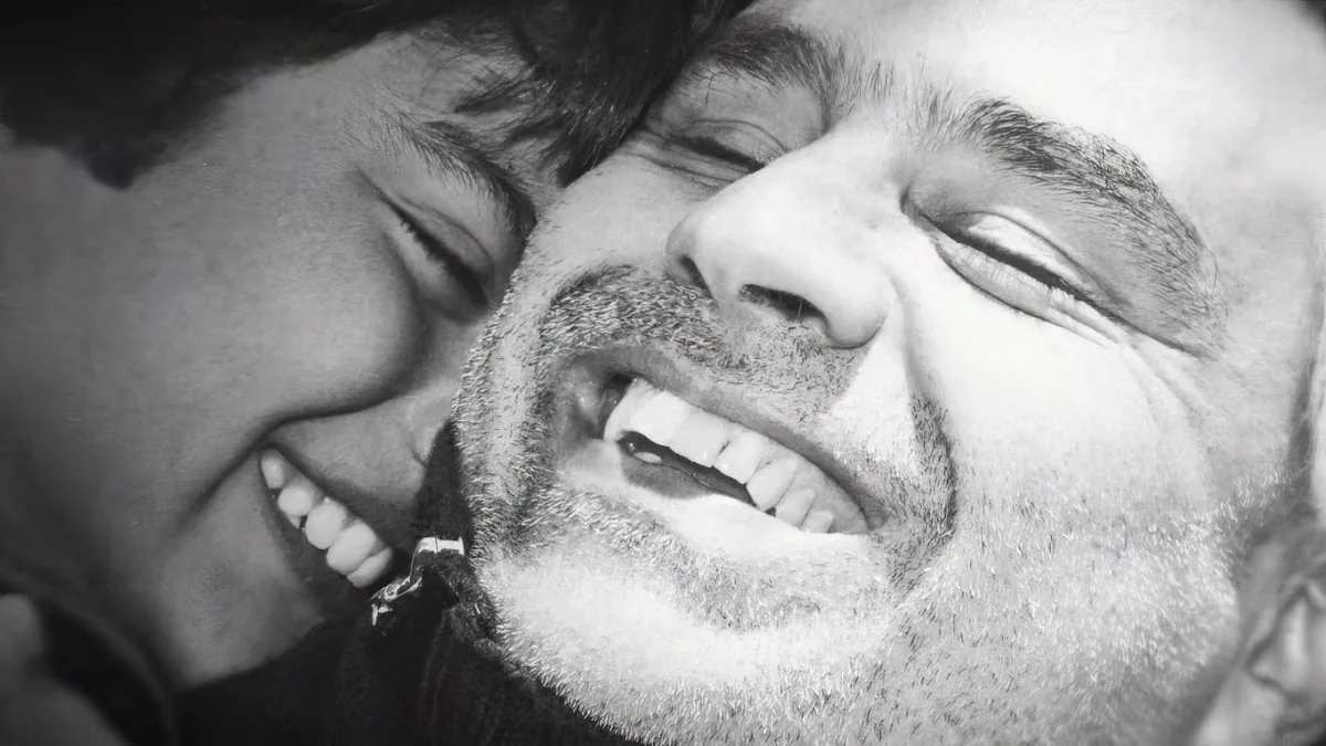 A man with a beard and mustache is being kissed on the cheek by another person.