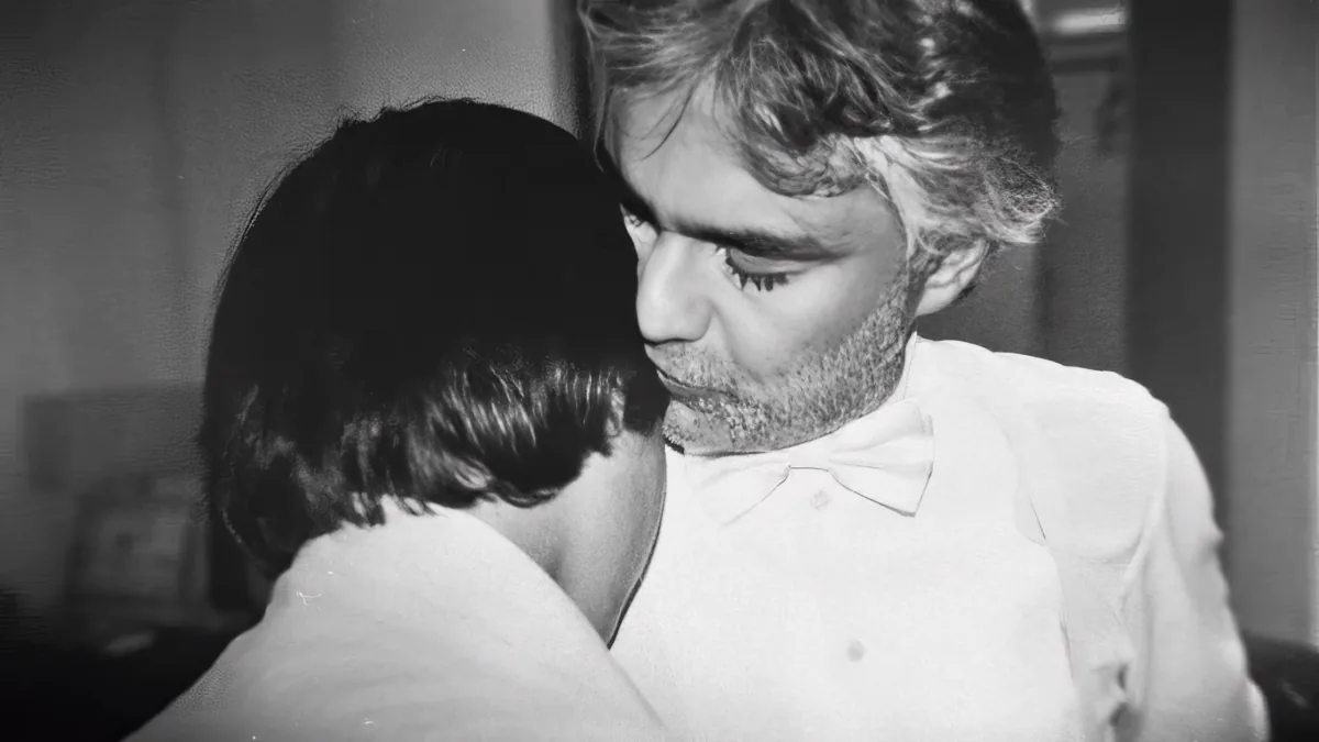 A man in a white shirt embraces a woman with dark hair, both appearing close and intimate.