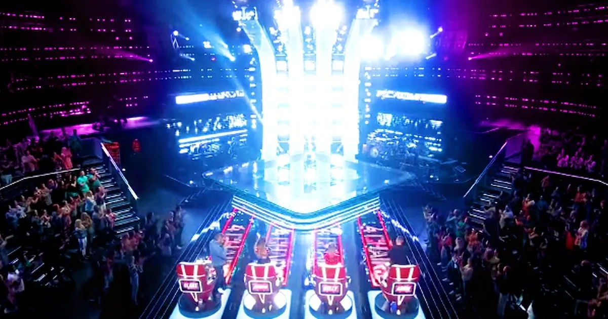 A vibrant stage with bright lights, judges' chairs, and a large audience in a lively setting.
