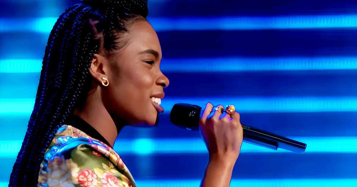 A woman with braided hair smiles while holding a microphone against a blue-lit background.