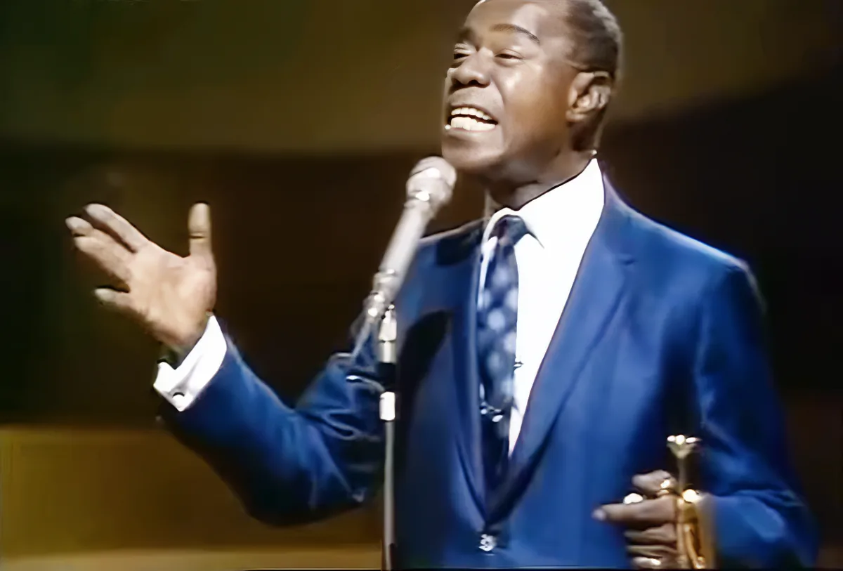 A man in a blue suit sings passionately into a microphone, his hand raised in a gesture of emotion.