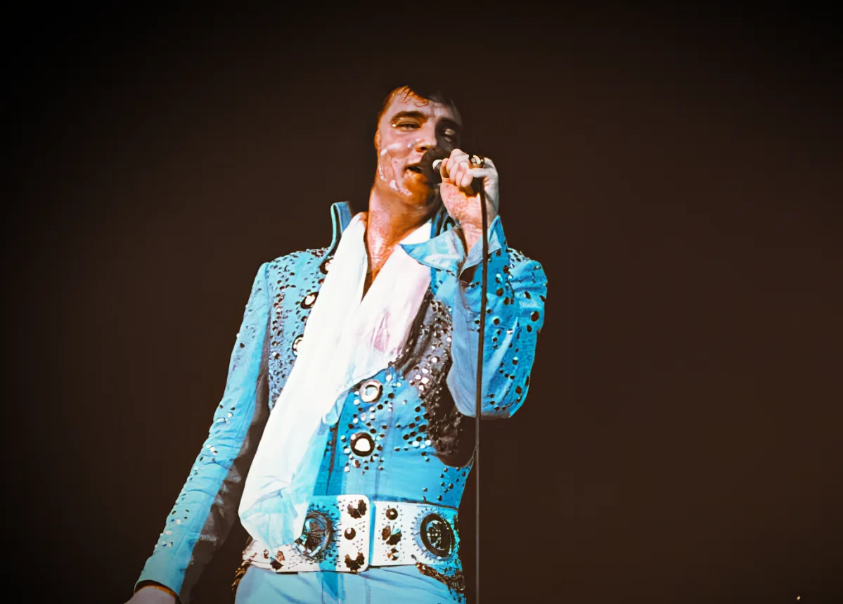Elvis Presley in a blue sequined suit singing on stage.
