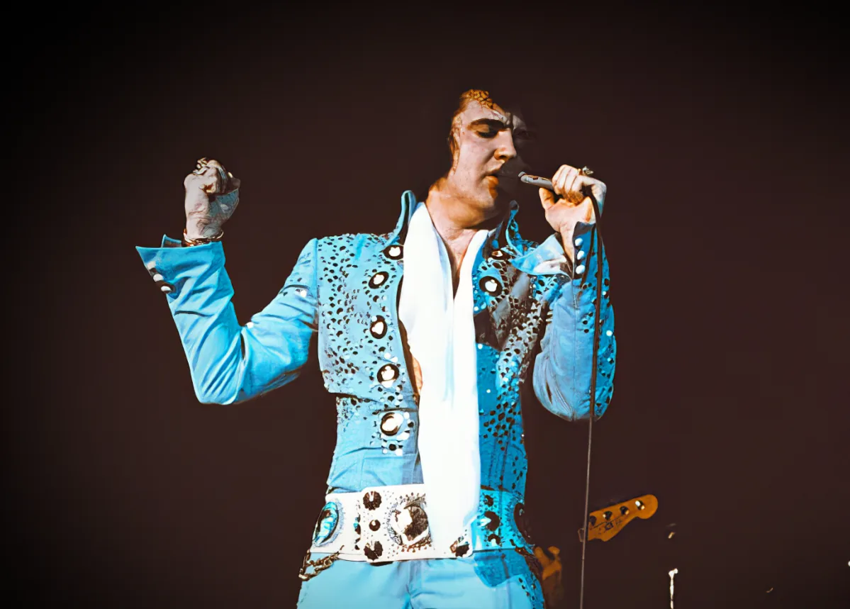 Elvis Presley in a blue sequined suit singing on stage.