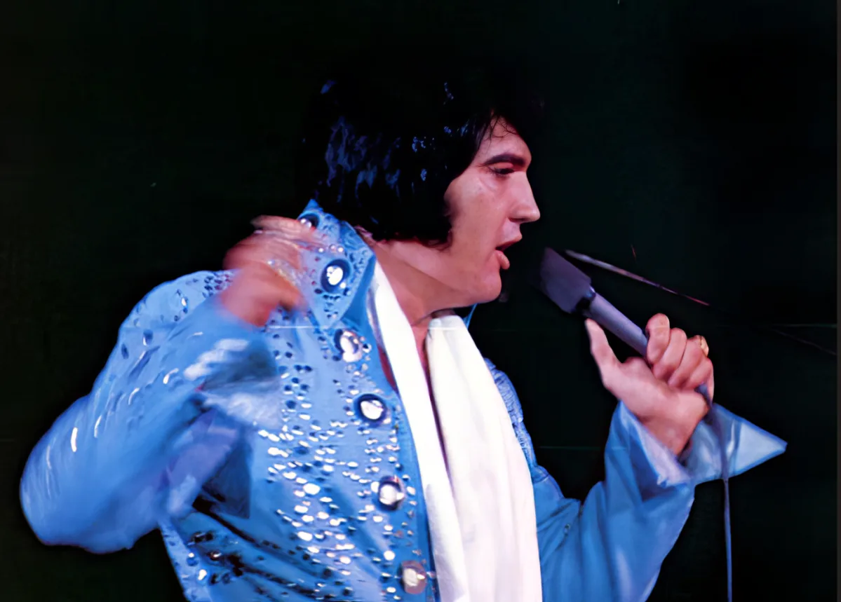 A performer in a blue sequined outfit is singing into a microphone, holding a piece of fabric.