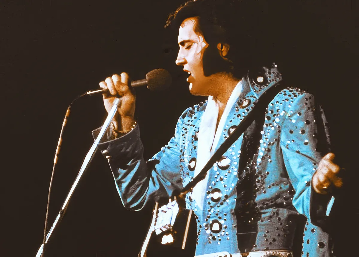A performer in a blue studded outfit sings into a microphone on stage.