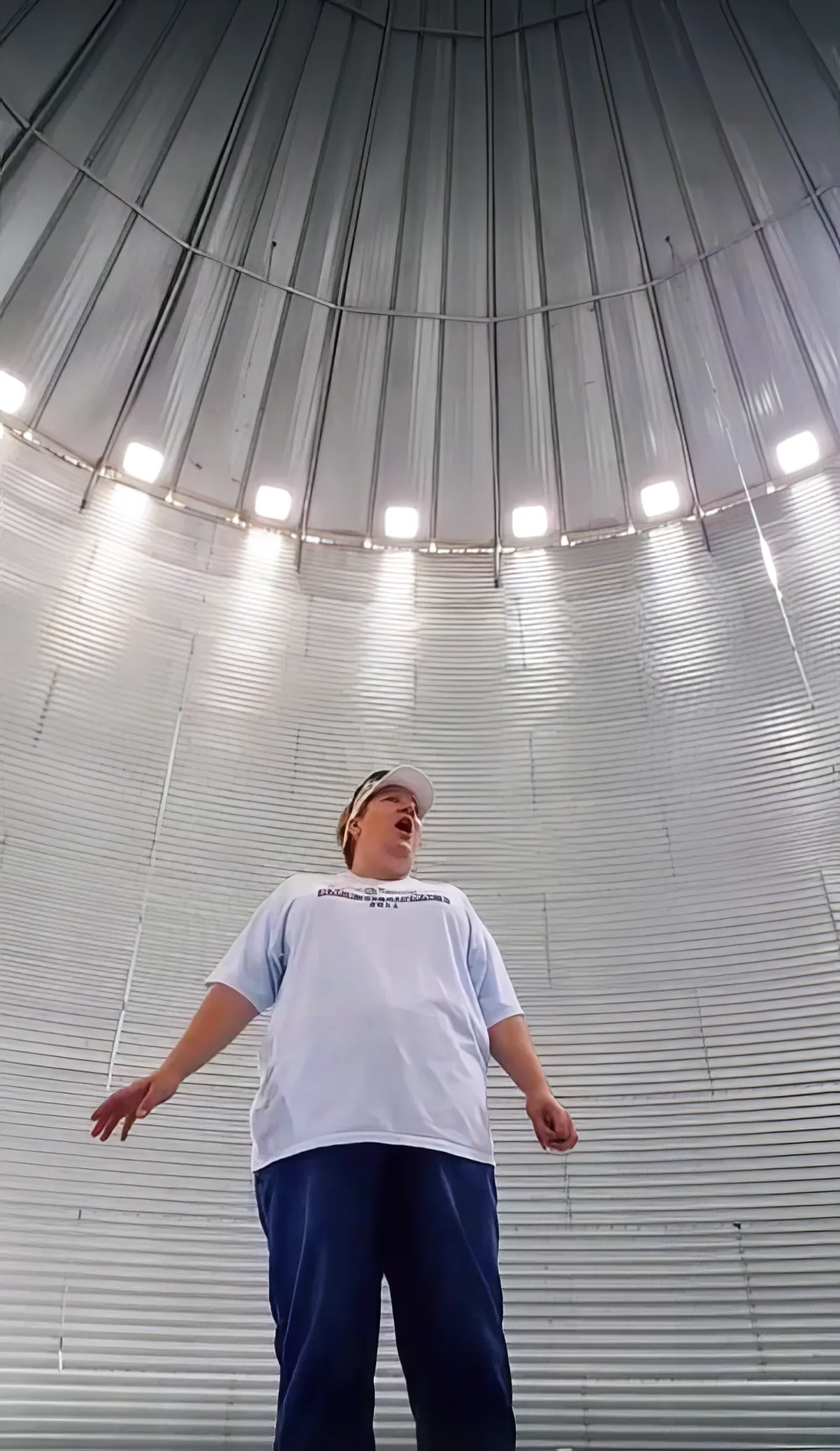 A person in a white shirt and blue pants stands inside a large, metallic, dome-shaped structure with bright lights.