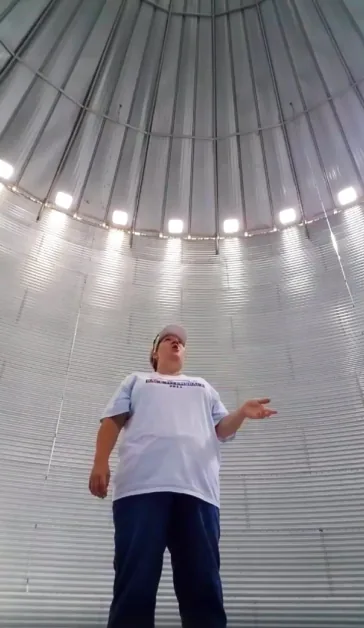 A person in a white shirt and cap stands in a large, metallic, dome-shaped structure with bright lights.