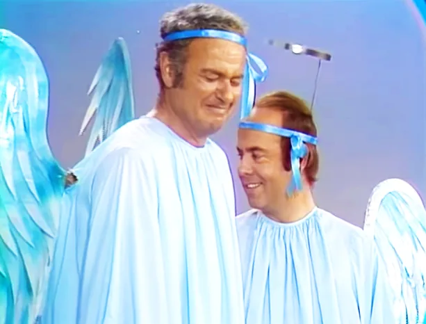 A man in a light blue robe and headband stands among others in similar attire, possibly in a performance or event.