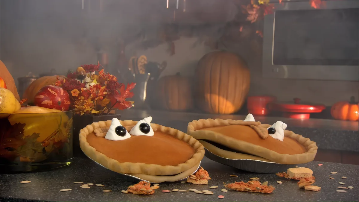 Pumpkin pies decorated as turkeys with meringue eyes and beaks, surrounded by autumn decorations and pumpkins.