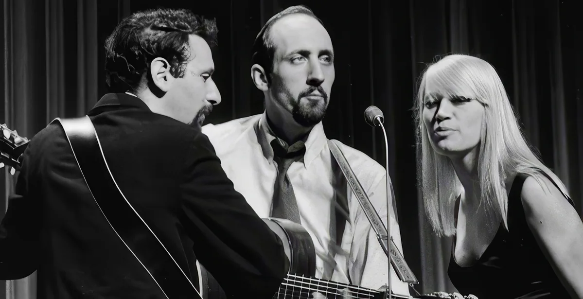 A man with a mustache and guitar is playing, surrounded by other musicians.