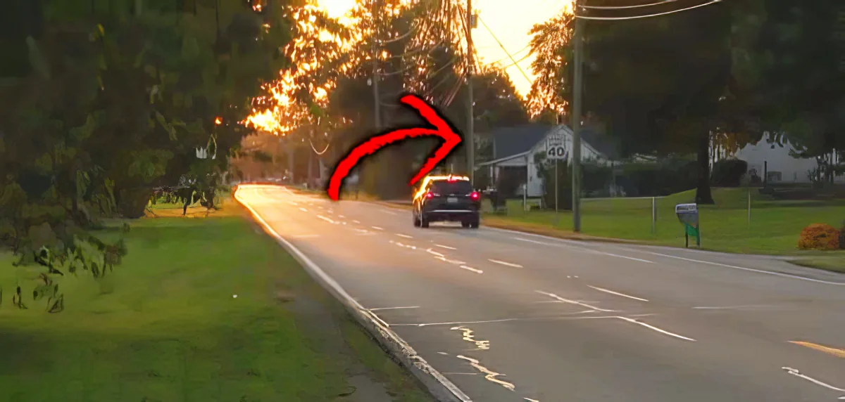 A car drives down a road at sunset, with a red arrow pointing to the vehicle.