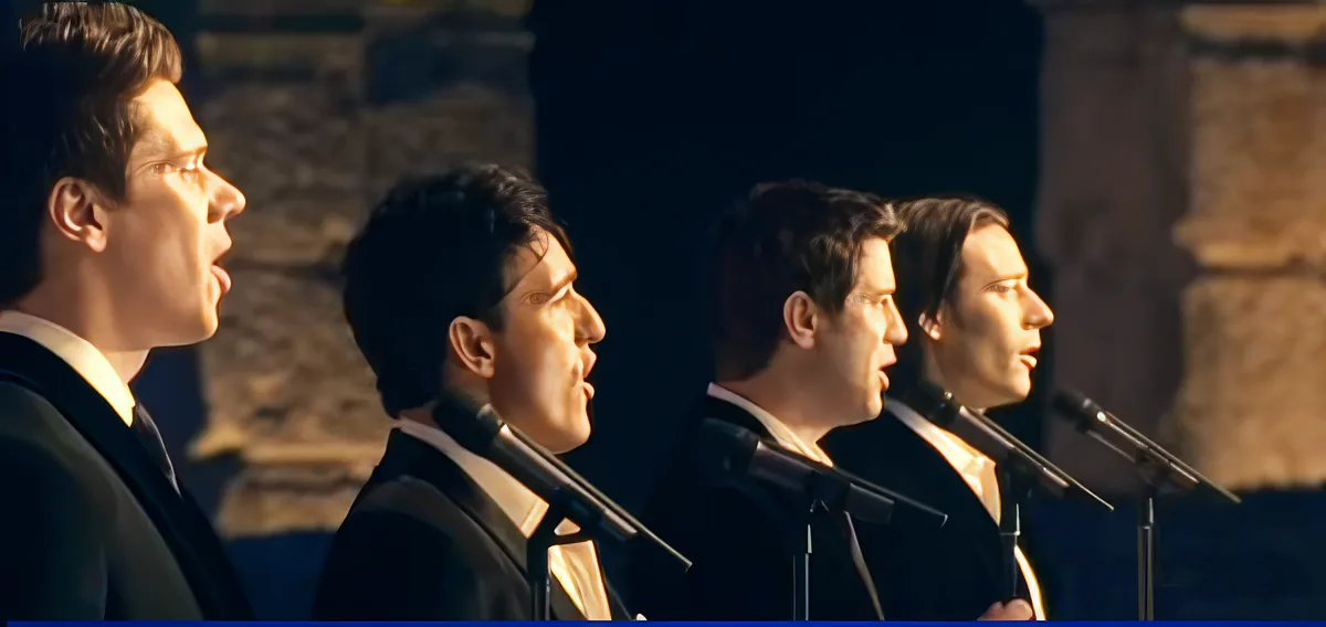 A group of men in formal attire singing into microphones, possibly in a choir setting.
