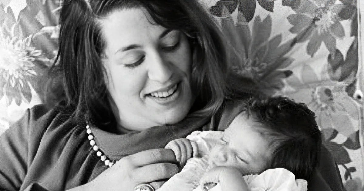 A woman holds a sleeping baby, both smiling, against a floral-patterned background.