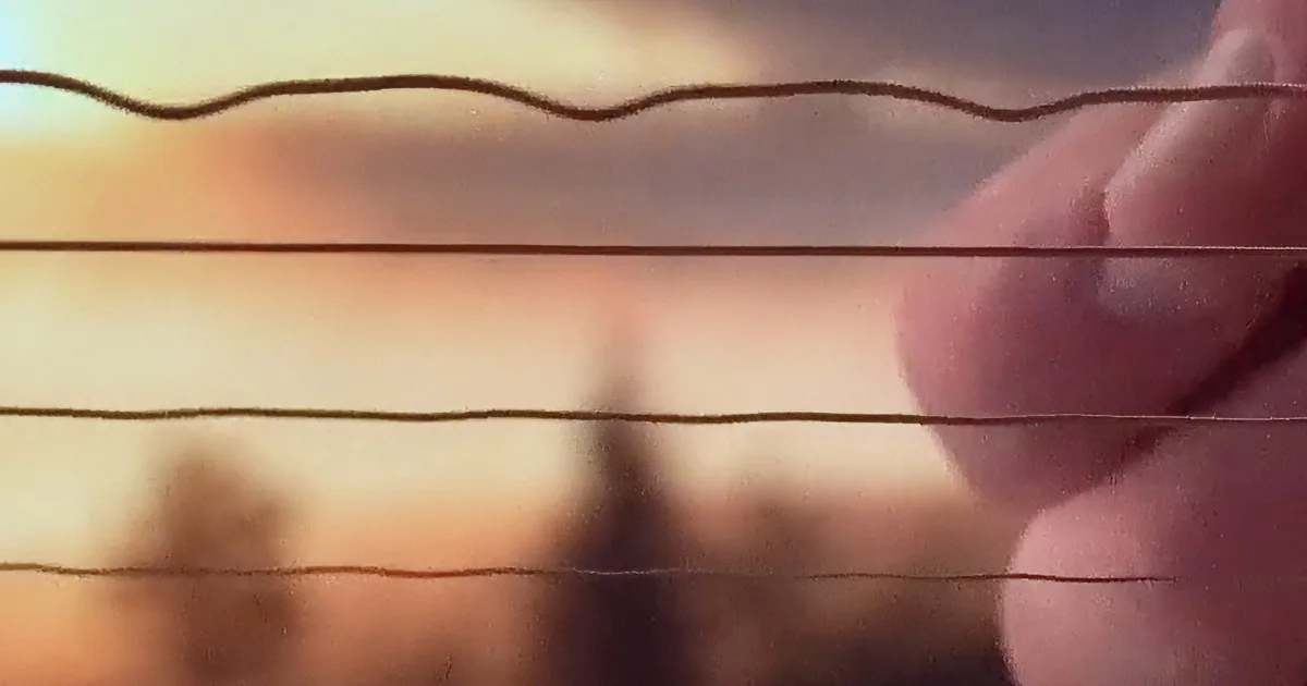 A hand holds a thin wire against a blurred background of trees and sky.
