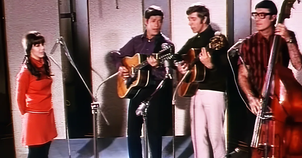 A woman in a red dress plays a guitar while a man in a black shirt sings into a microphone.