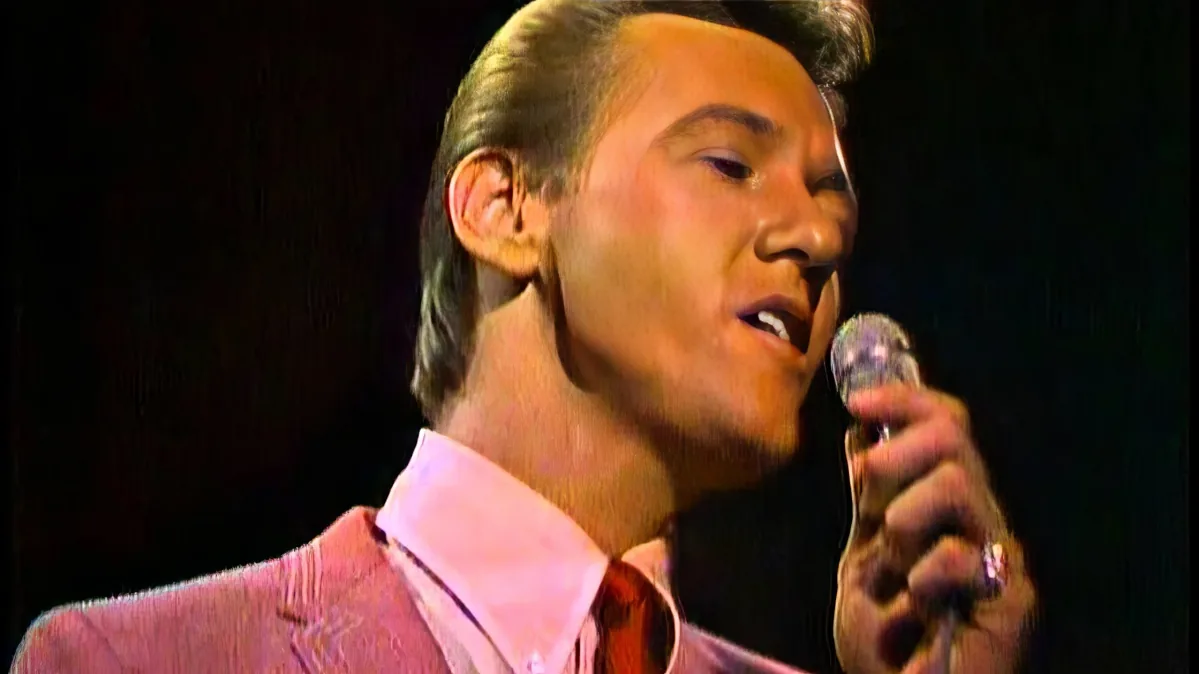 A man in a pink suit sings into a microphone, his expression focused and passionate.
