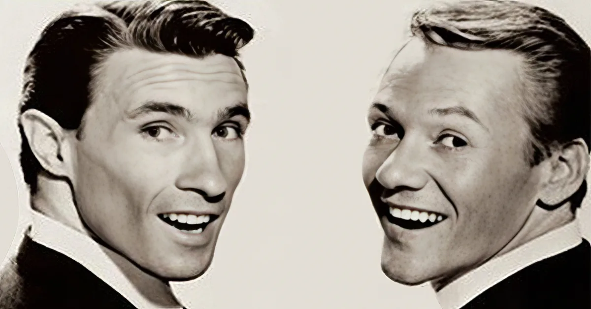 Two men in suits, both smiling, with one having a more pronounced smile.