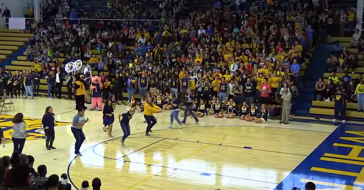 A group of people dancing on a basketball court with a cheering crowd in the background.