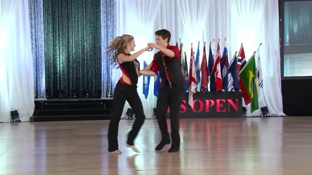 A couple dances energetically on a stage with flags and a banner in the background.