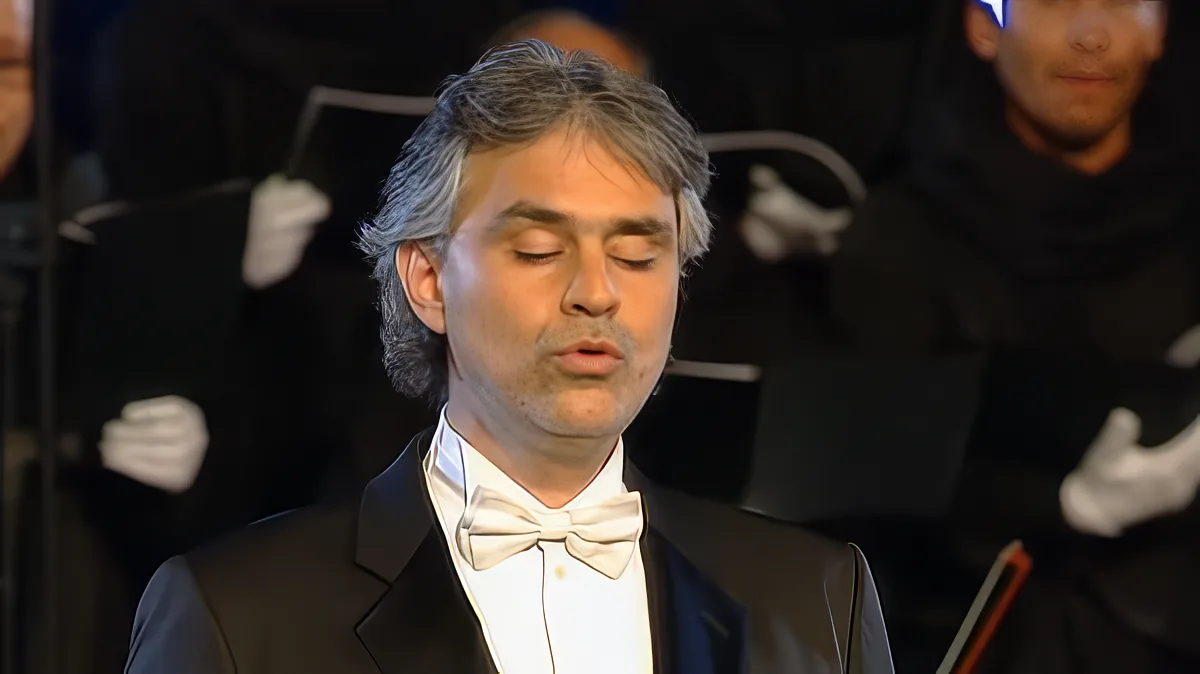 A man in a tuxedo with a bow tie, standing in front of an orchestra.