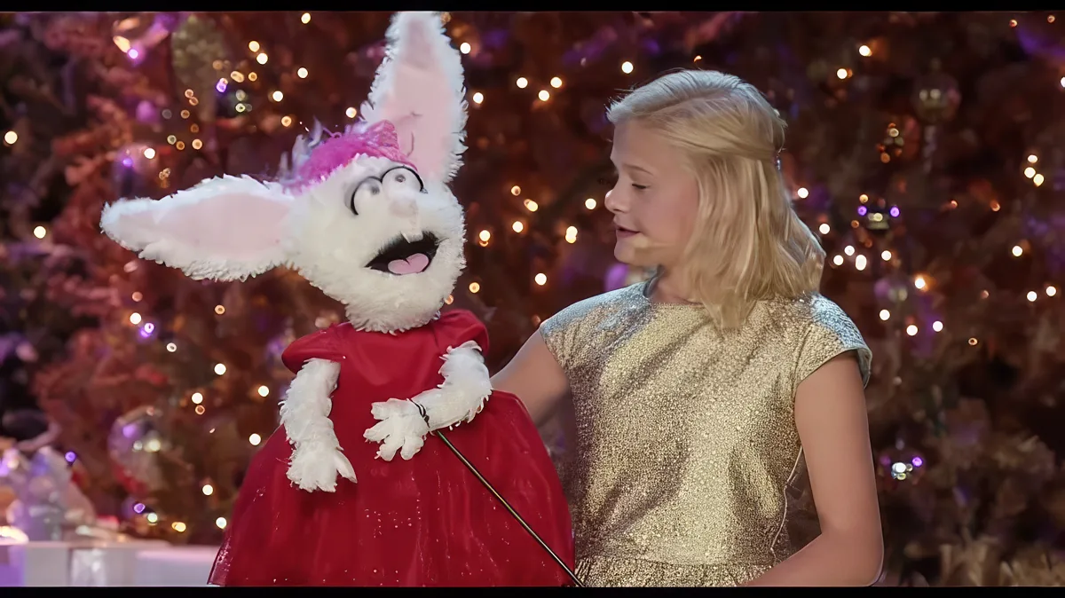 A young girl in a gold dress stands beside a person in a red and white bunny costume in front of a Christmas tree.