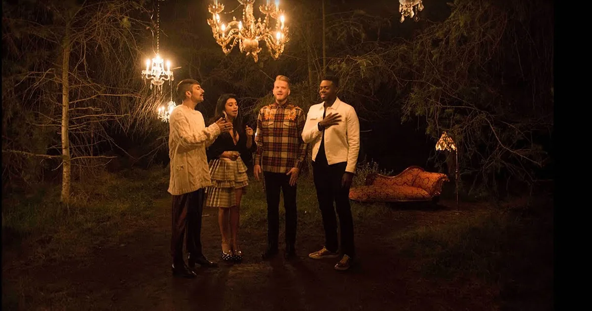 Four people stand in a dimly lit outdoor setting, surrounded by trees and chandeliers, creating a mysterious atmosphere.