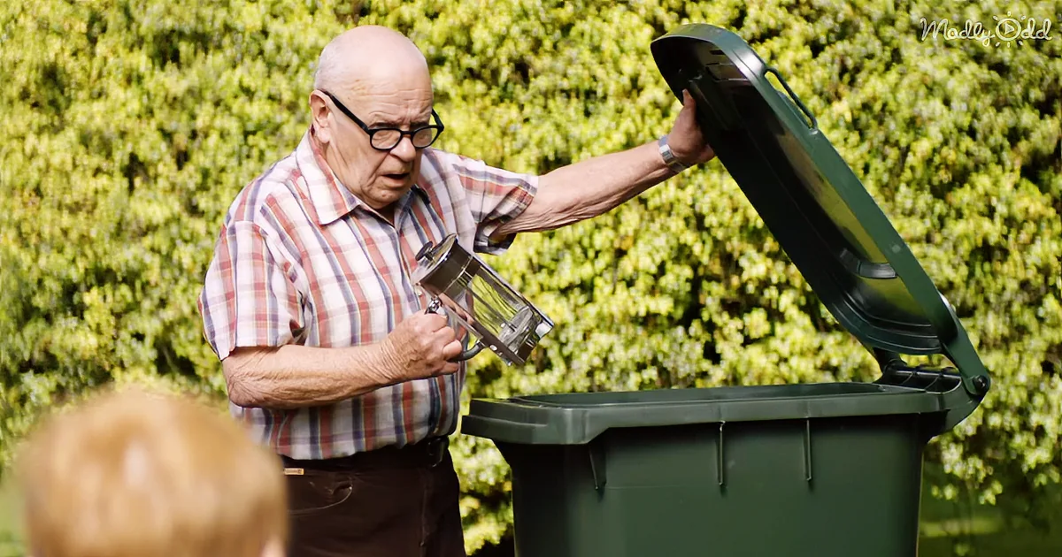 An older man in a plaid shirt pours something from a pitcher into a green trash can.