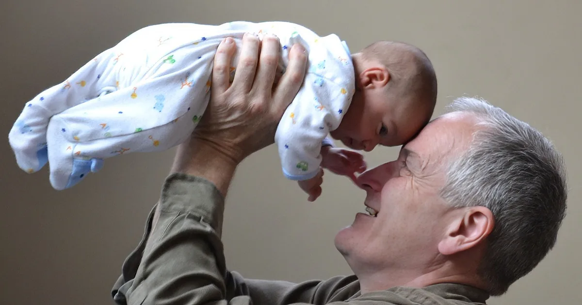 A man holds a baby above his head, both smiling, in a warm, intimate moment.