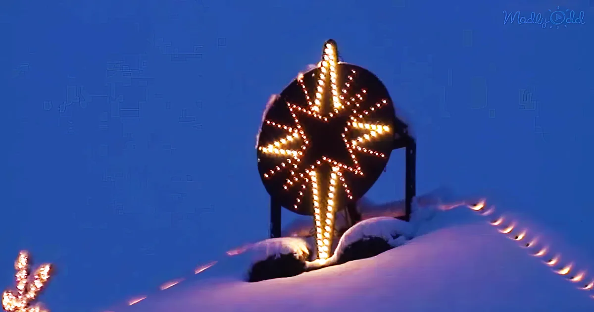 I see a large illuminated snowflake decoration on a snowy hill against a dark blue sky.