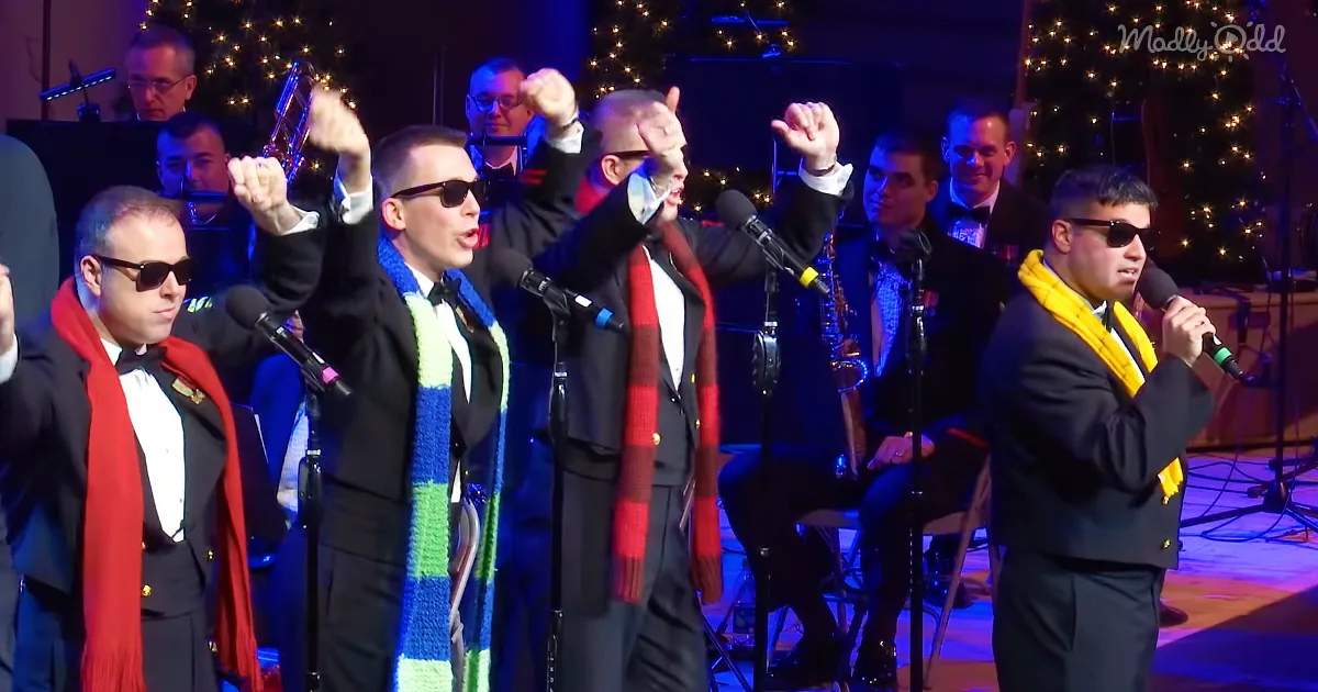 A group of men in suits and scarves sing into microphones, raising their fists in a festive setting.