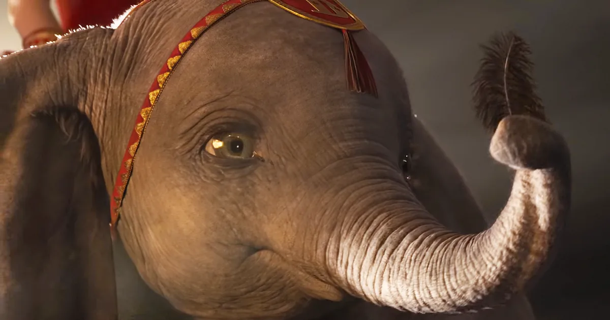 A close-up of a baby elephant adorned with a red and gold headband, raising its trunk.