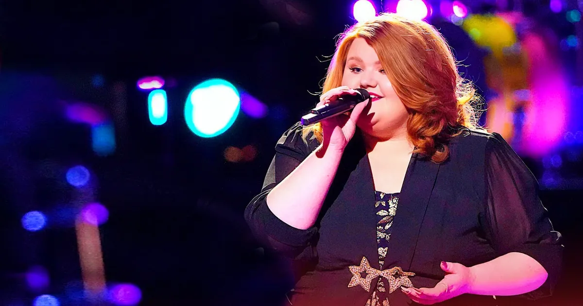 A woman with red hair sings into a microphone on a stage with colorful lights.
