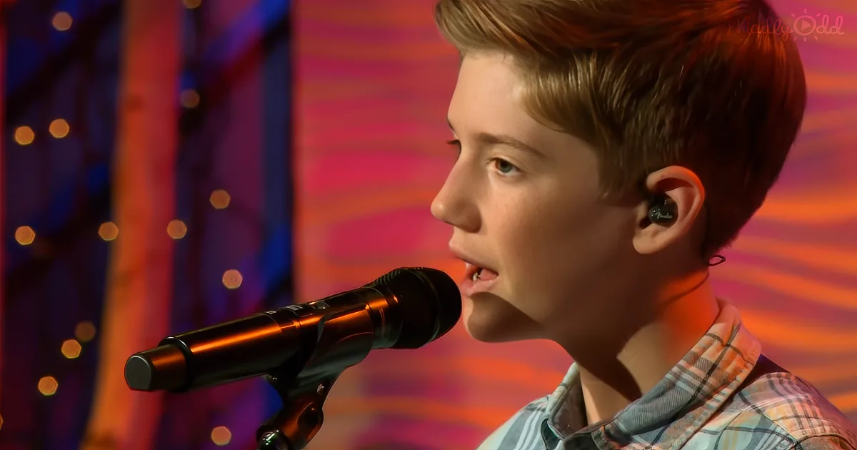 A young boy sings into a microphone, wearing a plaid shirt and earpiece, against a colorful backdrop.
