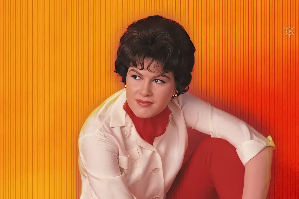 A woman in a white blouse and red scarf poses against a vibrant orange background.