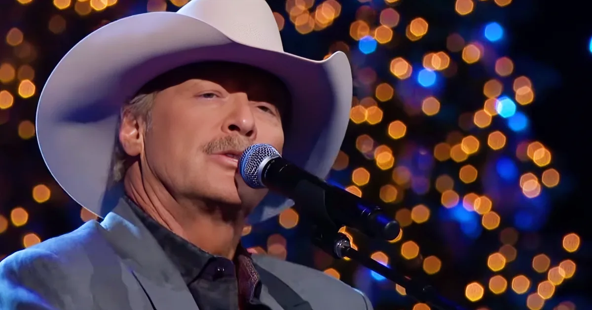 A man in a white cowboy hat sings into a microphone, surrounded by bokeh lights.
