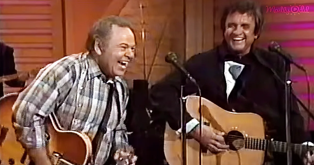 Two men, one in plaid shirt, the other in suit, both holding guitars and smiling.