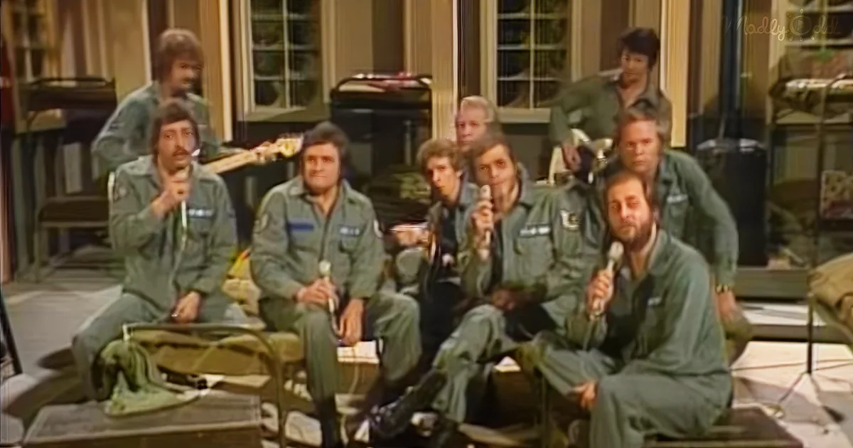 A group of men in green uniforms are singing into microphones on stage.