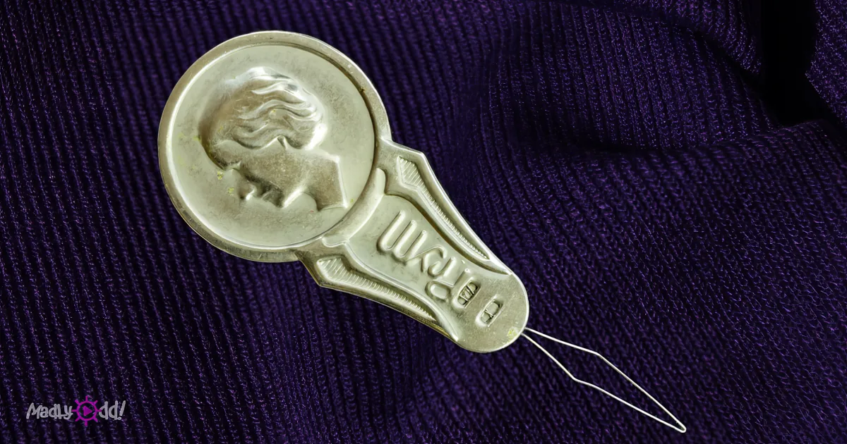 A metallic spoon with a woman's profile and the word "BERRY" on it lies on a purple textured surface.
